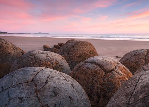 Tightly packed Moeraki Boulders under a colorful sky