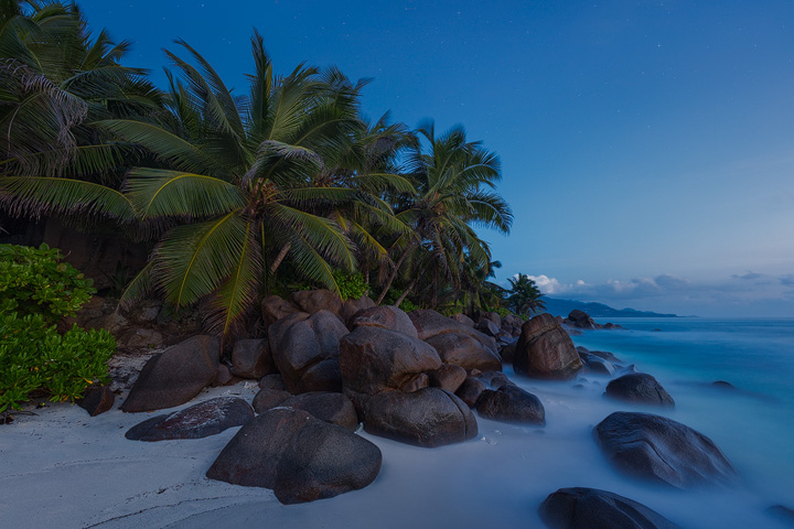 A blue starry sky over a secluded cove on Mahe