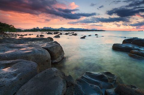 Rocky seashore at sunset with colorful clouds and calm water.