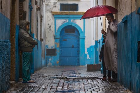 Two people stand in a narrow, rainy alley in Essaouira with blue-painted walls.
