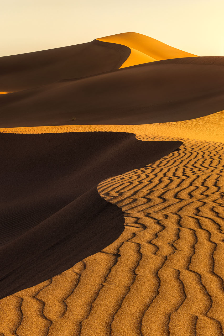 Golden light illuminates the dunes and structures of the Erg Chigaga