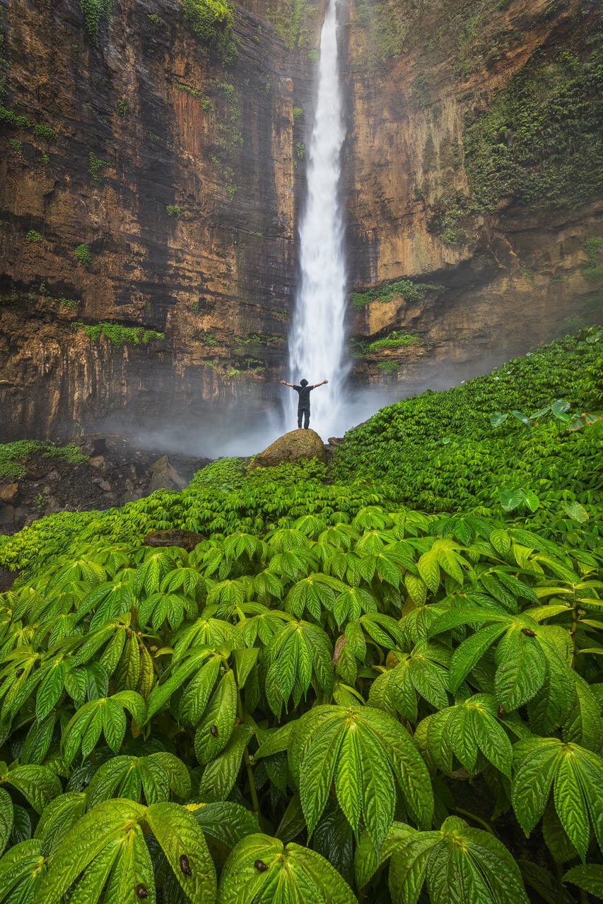 Ein Junge steht vor dem mächtigen Kapas Biru Wasserfall in Java