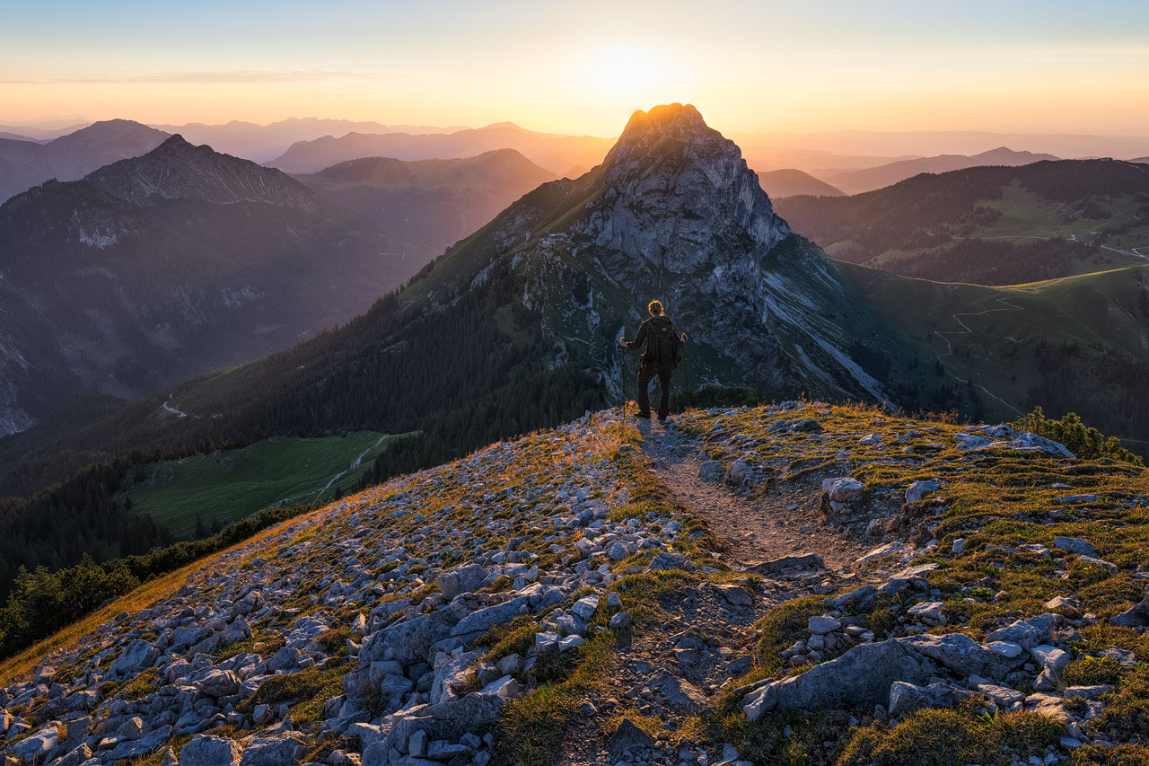 A hiker gazing toward the sun and the Aggenstein Mountain.