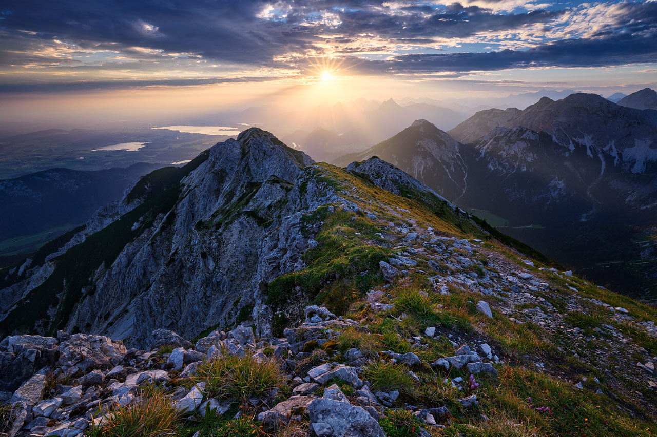 The sun rises above the Brentenjoch mountain with the Forggensee shimmering in the distance.