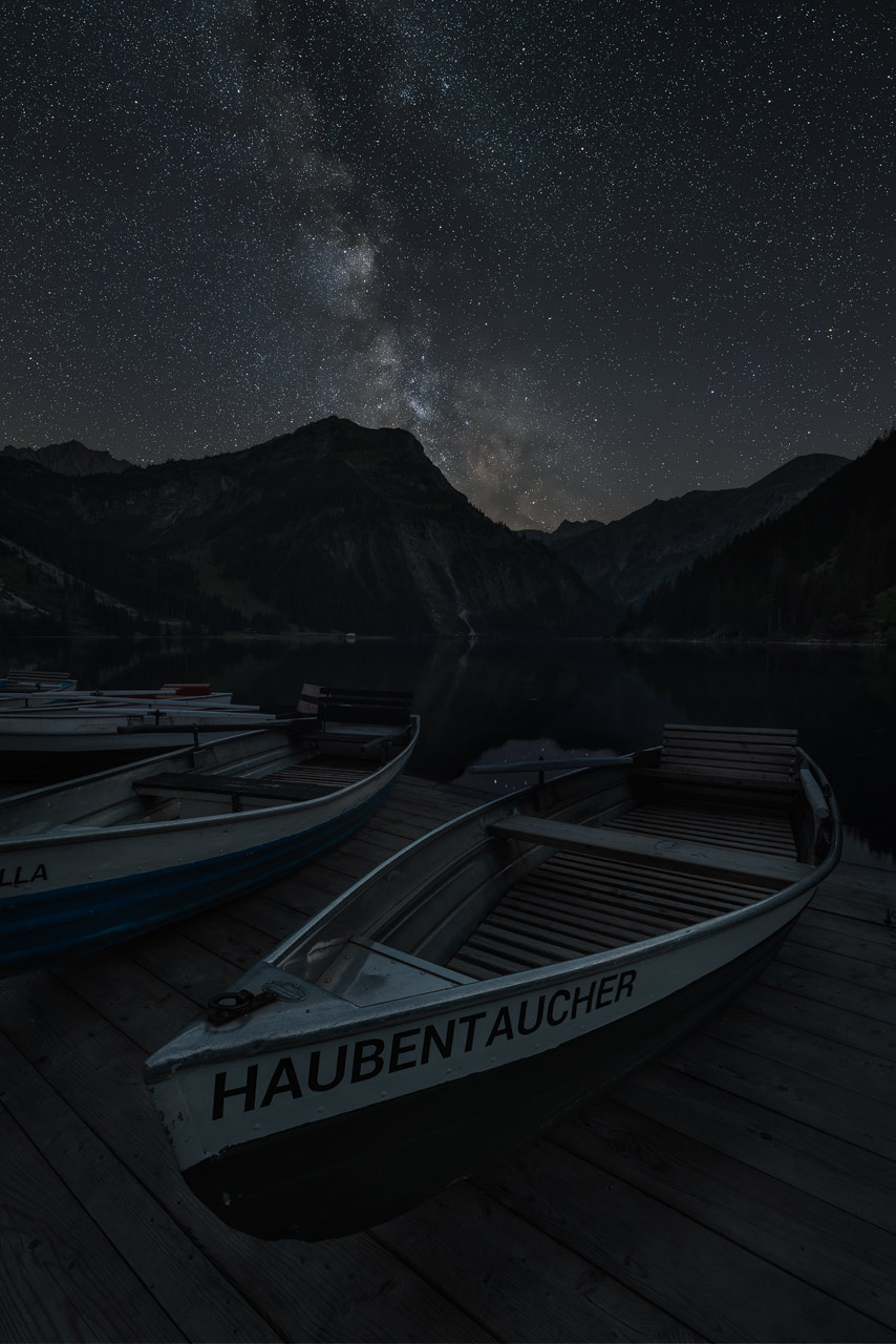 Boats at the shore of lake Vilsalpsee in Austria with the Milky Way above.