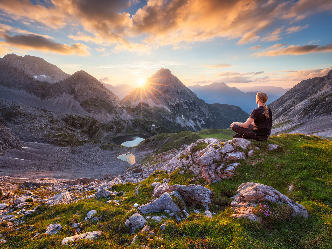 A person meditating in the Austrial mountains with the setting sun.