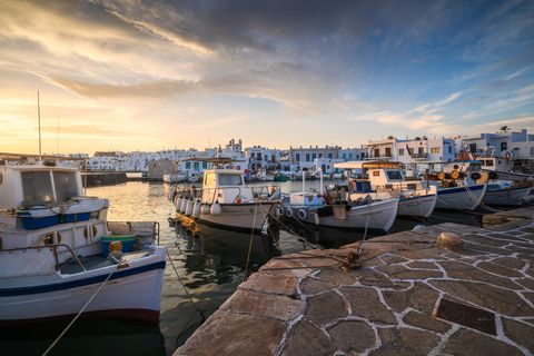 Fishing boats docked at the picturesque Naoussa harbor with traditional white buildings in the background at sunrise.
