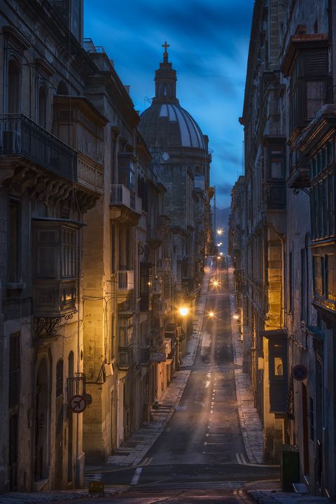 Narrow street in Valletta, Malta at dawn, lined with historic buildings and traditional balconies.