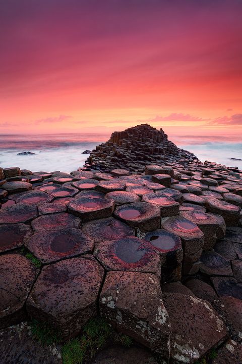 Hexagonal basalt columns of the Giant’s Causeway at sunset with a dramatic pink and orange sky.