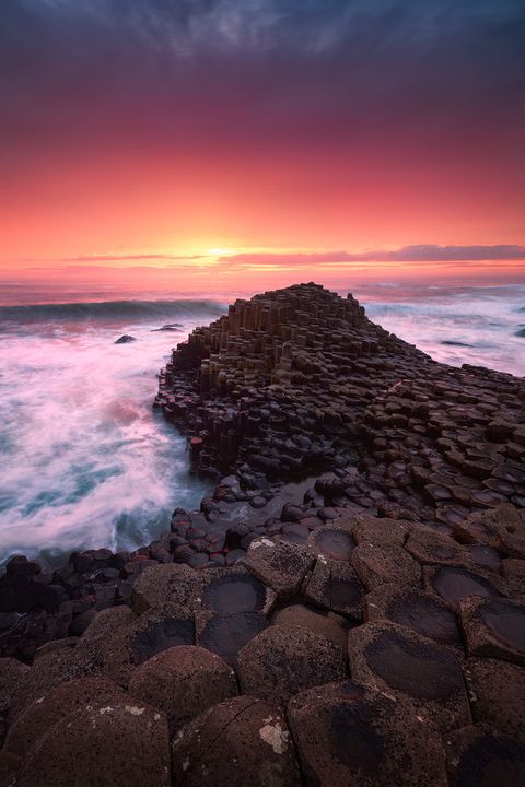 Sunset over the Giant’s Causeway with its distinctive hexagonal basalt columns and waves crashing along the rugged Northern Ireland coast.