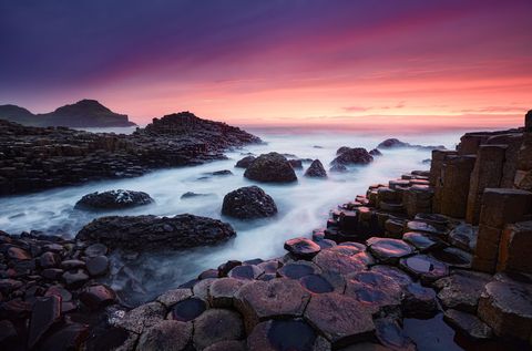 Hexagonal basalt columns of the Giant's Causeway after sunset with misty waves and colorful sky in Antrim, Northern Ireland.
