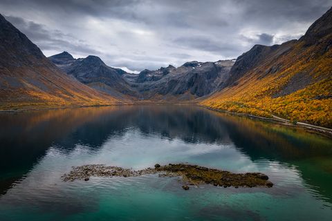 Grotfjord surrounded by steep rocky mountains and forests with vibrant autumn foliage under a cloudy sky in Norway.