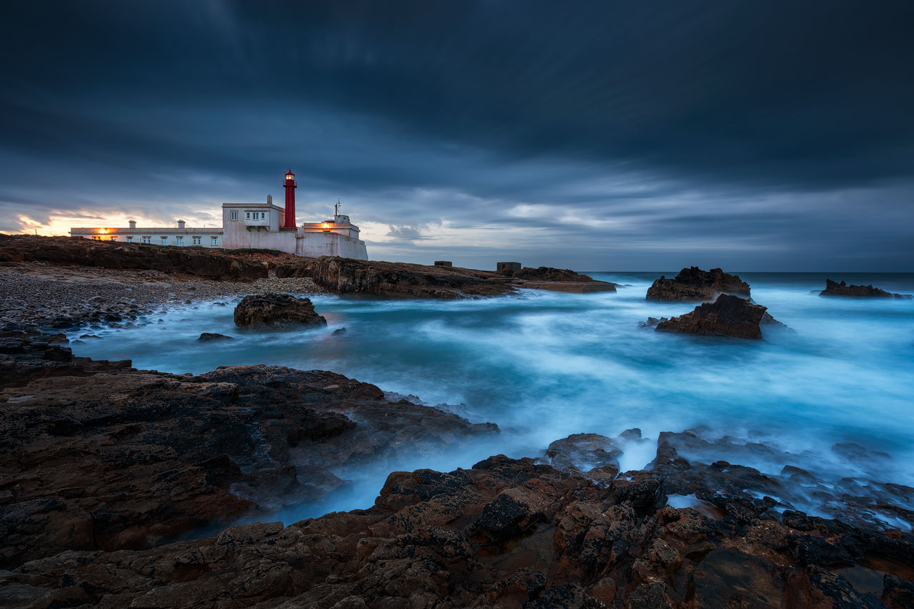 A lighthouse facing the stormy sea on a rocky shore