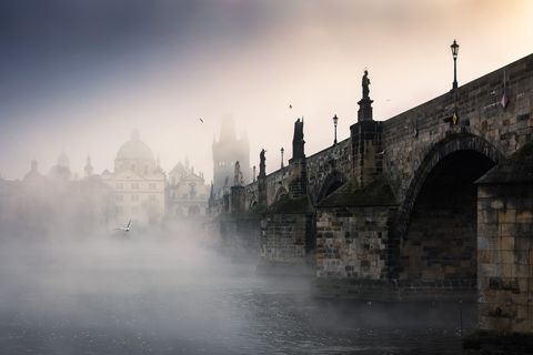 Die Karlsbrücke über die Moldau in Prag, gehüllt in morgendlichen Nebel, mit Statuen und alter Stadtarchitektur im Hintergrund.