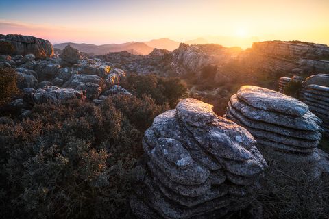 Sunrise over El Torcal de Antequera with dramatic limestone rock formations and scattered shrubs in southern Spain.