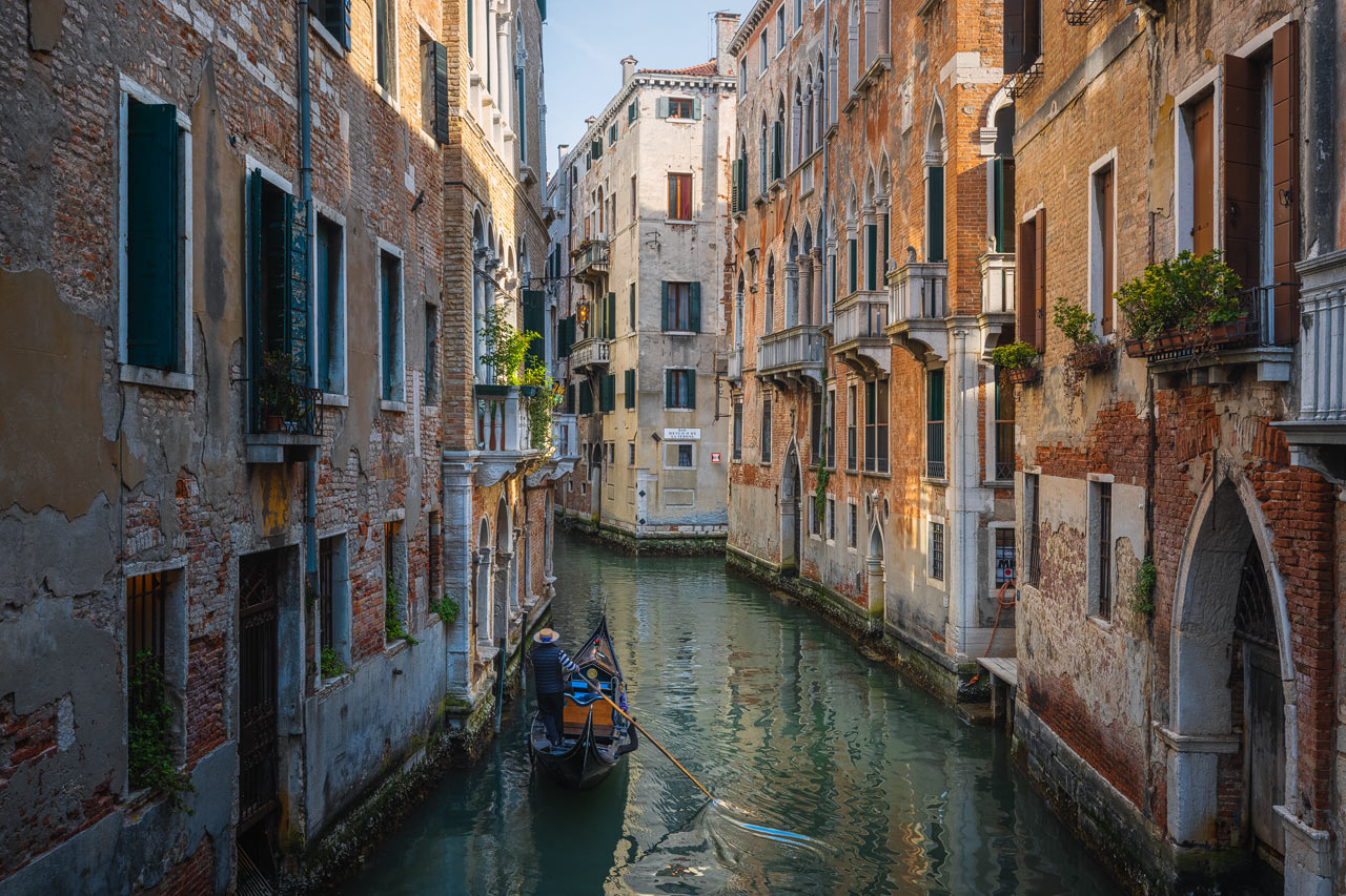 A gondolieri navigates his gondola through a canal in Venice