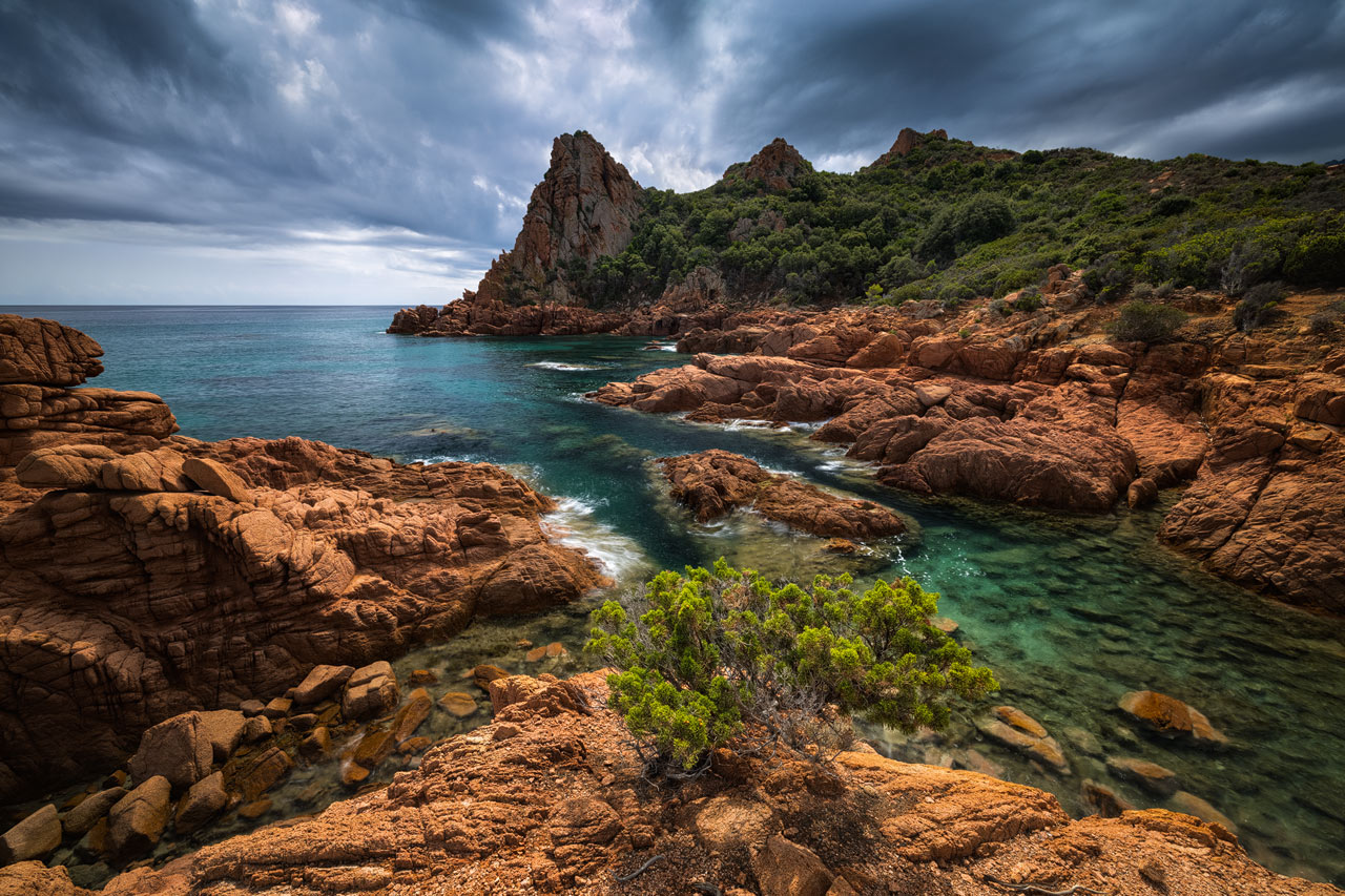 Rote Felsen, tief blaues Wasser und üppige Vegetation an Italiens Küste.