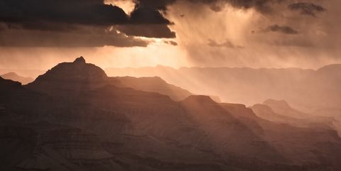 Sunrise over the Grand Canyon with dramatic clouds and sunbeams illuminating the rocky landscape.